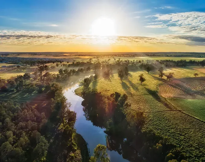 Aerial image of sunrise over river with views out over the land encompassing paddocks and bush.